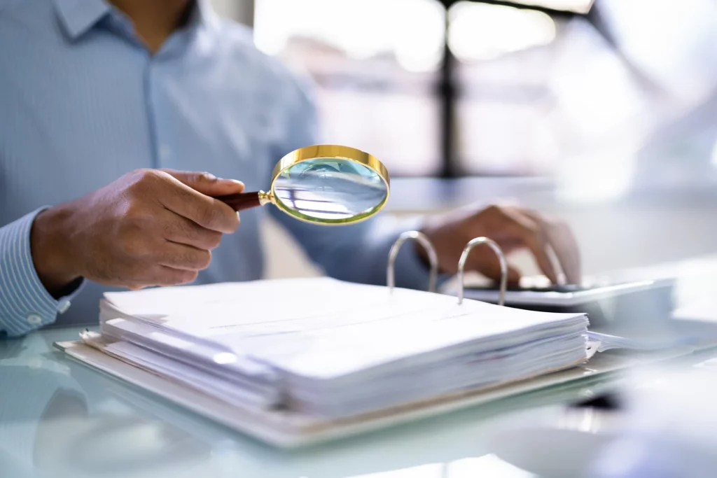 Lawyer Using A Magnifying Glass To Inspect A Binder Of Documents.